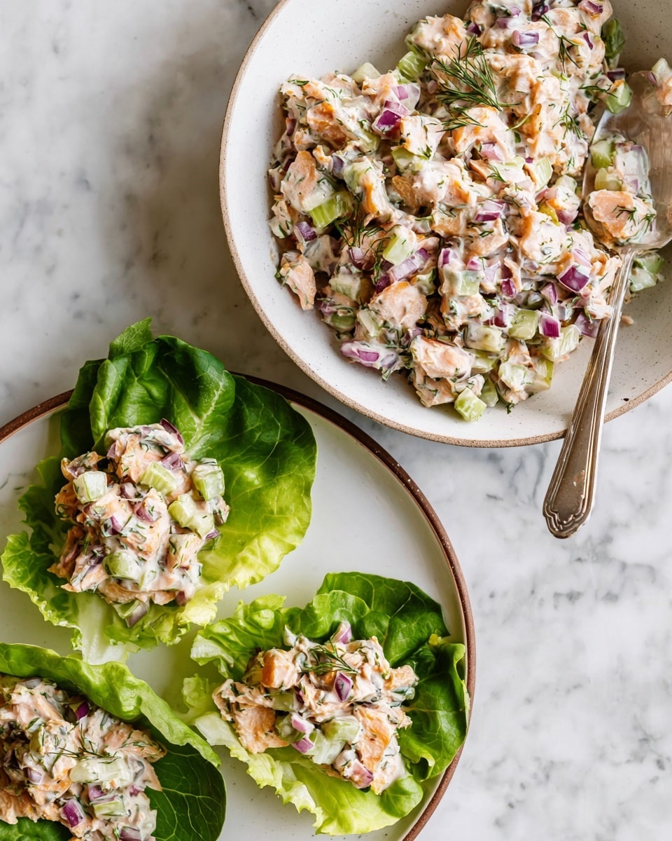 A white bowl filled with a layered mix of cooked pink salmon pieces, finely chopped green celery, and small bits of red onion scattered all over. The dish is lightly sprinkled with fresh green dill on top, and there is a creamy white sauce mixed through it. A white spoon rests inside the bowl on the right side. The bowl sits on a white marbled surface with fresh dill sprigs in the top right corner, and a small round bowl with more sauce and a spoon nearby. Photo taken with an iphone --ar 4:5 --v 7