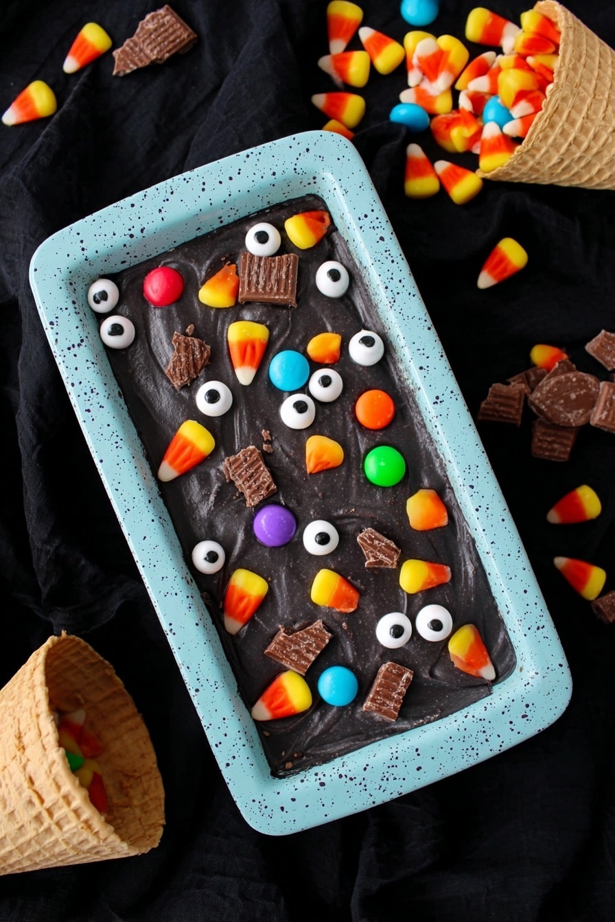 Boo Batter No-Churn Ice Cream, no-churn black ice cream, Halloween ice cream recipe, easy no-ice-cream-maker ice cream, fun party dessert - A rectangular dish with a light blue speckled container holds a smooth, dark black surface of dessert. On top, there are scattered small white candy eyeballs with black centers, colorful round candy pieces in orange, yellow, green, red, and purple, pieces of candy corn with yellow, orange, and white layers, and broken sections of chocolate wafer candy bars. The scene is against a black fabric background with two waffle cones spilling colorful candy wrappers and candy into the frame. photo taken with an iphone --ar 2:3 --v 7