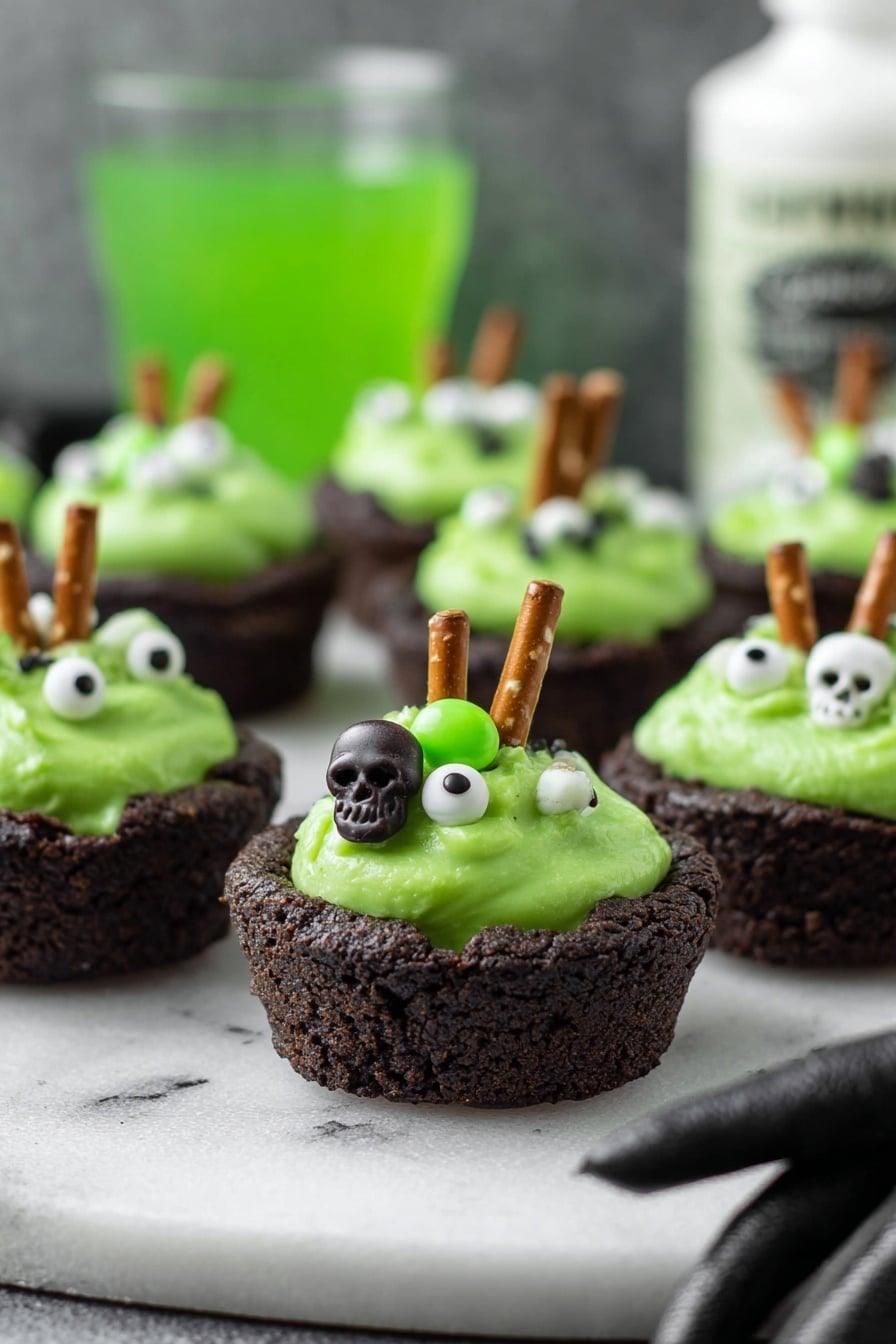 Cauldron Cookie Cups, Halloween Cookie Cups, Whimsical Dessert Recipes, Chocolate Cookie Cups, Spooky Treats for Parties - The image shows small dark brown cookie cups filled with bright green creamy frosting. Each frosting has small white and green candy decorations shaped like skulls and eyeballs, giving a spooky look. A small pretzel stick is inserted into the frosting on each cup, standing upright. The cookie cups are placed on a white marbled surface, and in the background is a blurry green drink and a white bottle with black text. A woman's hand in a black glove is reaching towards the cookie cups from the right side. photo taken with an iphone --ar 2:3 --v 7