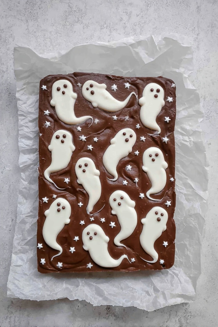 Halloween 3 Ingredient Ghost Bark, easy Halloween treats, no-fuss spooky desserts, quick ghost bark recipe, simple Halloween party snacks - A rectangular chocolate fudge layer placed on crinkled white parchment paper on a white marbled surface, decorated with multiple small white ghost shapes spread across the top. The ghosts are made from a white creamy layer, each with rounded heads and flowing tails with small dark eyes and mouths, giving a spooky look. Small white star-shaped sprinkles are scattered evenly across the chocolate background, adding texture and contrast. The overall look is smooth with a few swirled edges on the ghost shapes, making a playful Halloween-themed treat. photo taken with an iphone --ar 2:3 --v 7
