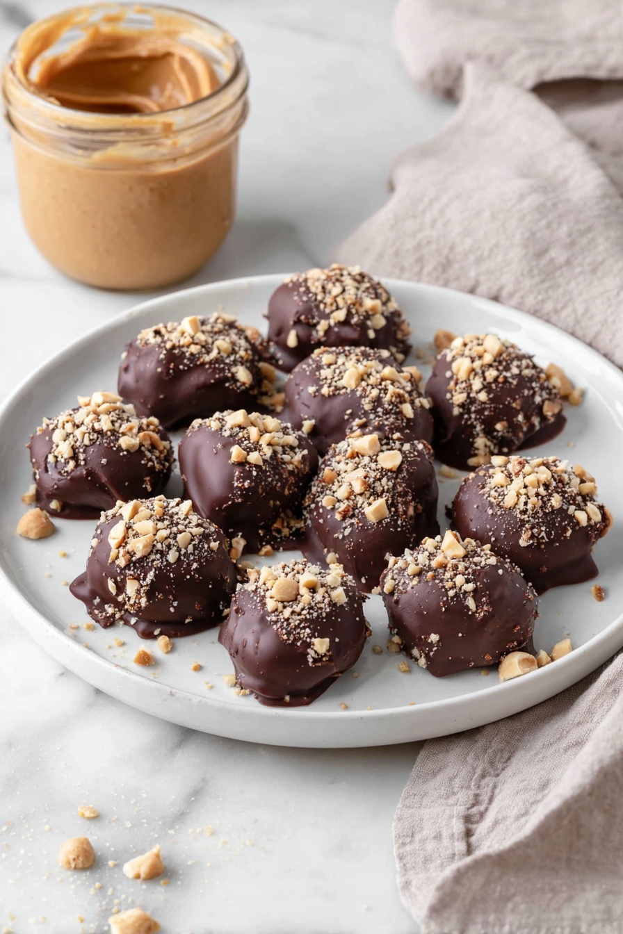 Date Snickers, healthy chocolate date bars, easy no-bake treats, chewy date snacks, peanut butter date bites - A white plate holds eleven bite-sized treats, each covered in a thick, dark brown chocolate layer with a slightly glossy and smooth texture. On top of each piece, there is a sprinkling of small, light tan chopped nuts adding a rough, crunchy texture. The treats are arranged loosely close to each other in the center of the plate. In the background, there is an open jar filled with smooth, creamy peanut butter in a light brown shade, and a light beige cloth with a soft, woven texture lies nearby on a white marbled surface. Photo taken with an iphone --ar 2:3 --v 7