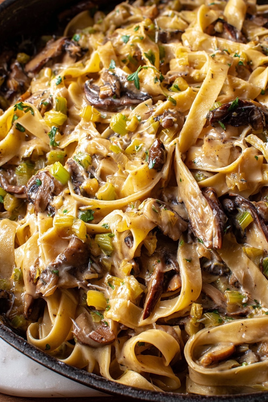 Caramelized Leek and Mushroom Pasta, leek and mushroom pasta, caramelized leek recipe, mushroom pasta with creamy sauce, comforting vegetable pasta - This close-up image shows a pan full of creamy pasta with broad, flat noodles tangled among large, uneven pieces of dark brown mushrooms. The sauce is light beige and coats the pasta and mushrooms, with small diced bits of green and yellow vegetables spread throughout, adding texture and color. The surface below the pan has a white marbled texture visible on the edges. photo taken with an iphone --ar 2:3 --v 7