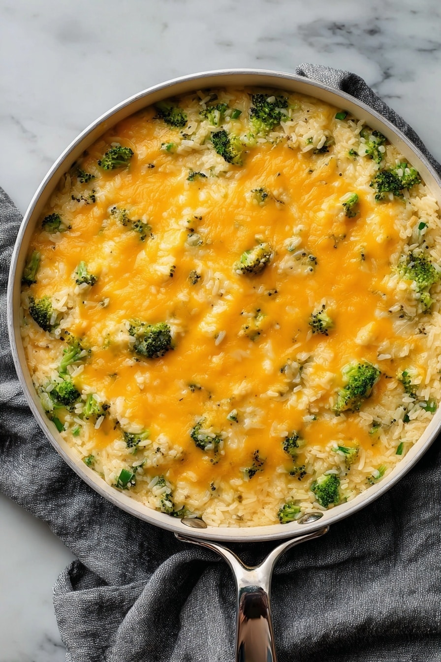 Cheesy Broccoli Rice Vegan Casserole, vegan cheesy broccoli casserole, plant-based broccoli rice bake, dairy-free cheesy casserole, vegan comfort food recipes - The dish is served in a round white pan with a silver handle, placed on a gray cloth over a white marbled surface. It has two main layers: the bottom layer is a mix of cooked white rice with small pieces of broccoli, giving a textured base of green and white. The top layer is a smooth, even spread of melted orange cheese covering the rice and broccoli, with small bits of broccoli peeking through. The cheese looks soft and slightly shiny, adding a creamy contrast to the grainy rice below. photo taken with an iphone --ar 2:3 --v 7