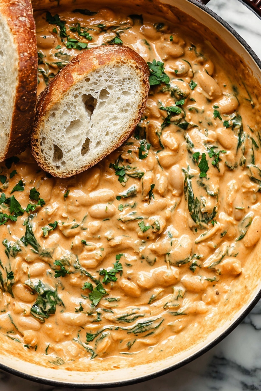 Creamy Sun-Dried Tomato Butter Beans with Basil and Spinach, vegetarian creamy bean dish with sun-dried tomatoes, healthy butter beans recipe with basil, quick vegetarian dinner, easy plant-based meal - A close-up image of a thick, creamy dip with a light orange color, filled with visible bits of chopped green herbs and small red pieces scattered throughout. Two slices of crusty white bread rest partially dipped on the surface of the mixture, showing a soft, airy texture inside the bread. The dip has a rich, smooth texture with swirls and folds, spread in a white bowl. The background features a white marbled surface. photo taken with an iphone --ar 2:3 --v 7