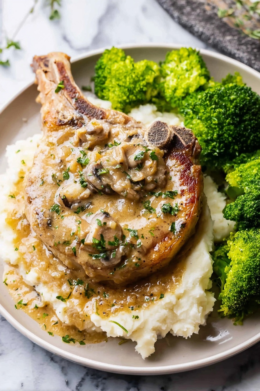 Easy Smothered Pork Chops, delicious pork chop dinner, comforting pork chop recipe, tender pork chops with gravy, simple pork chop meal - A large cooked pork chop sits in the center of a white plate on a bed of creamy mashed potatoes as the bottom layer; the pork chop has a light brown color with a creamy mushroom sauce on top, dotted with pieces of mushrooms and sprinkled with small green herbs; to the right side of the plate, there are bright green steamed broccoli florets with a slightly wet texture; the white mashed potatoes have a soft, slightly lumpy texture, and both the pork chop and sauce have a glossy sheen from the sauce; the plate sits on a white marbled surface; photo taken with an iphone --ar 2:3 --v 7