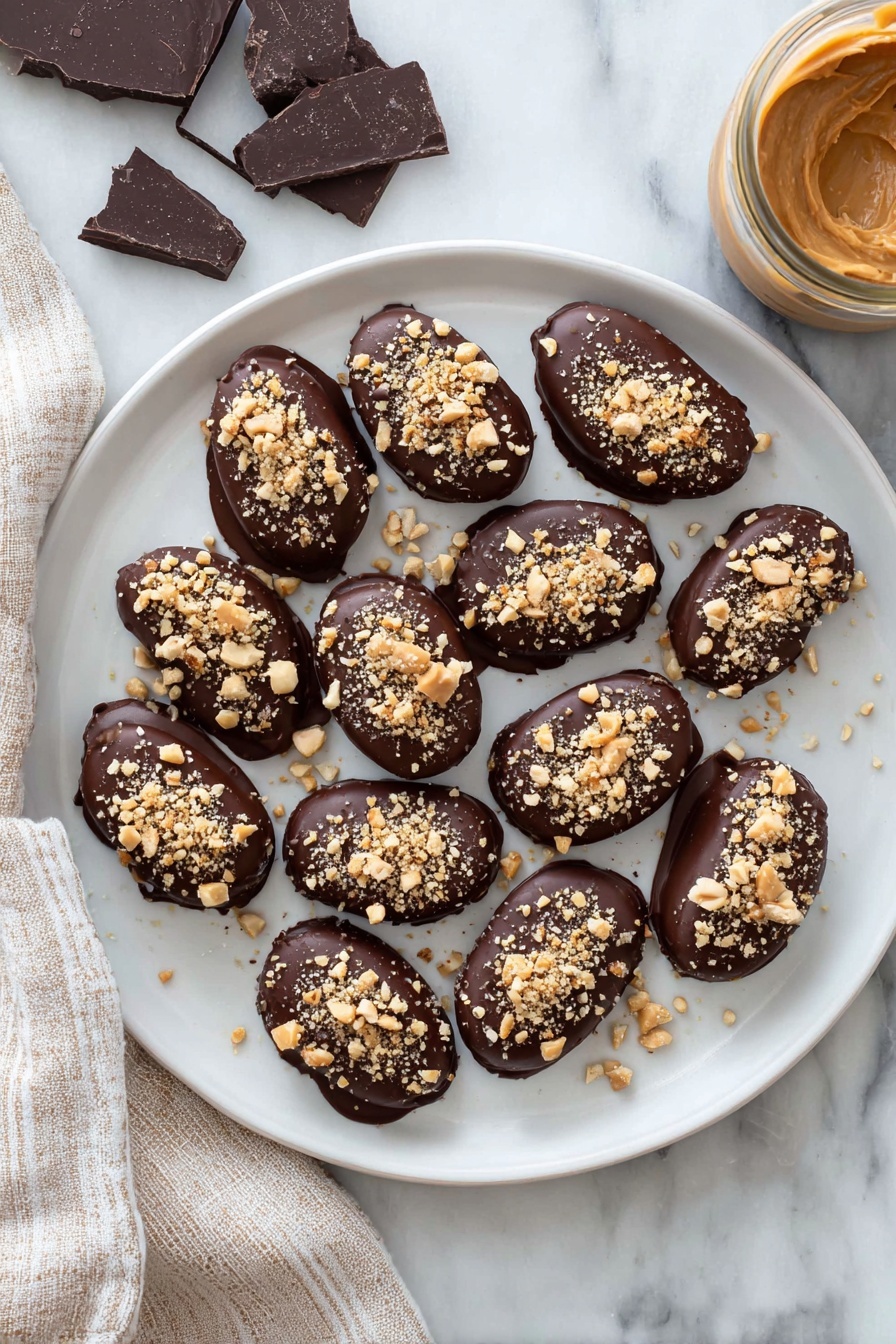 Date Snickers, healthy chocolate date bars, easy no-bake treats, chewy date snacks, peanut butter date bites - A white plate holds a dozen small oval treats, each fully covered in smooth dark chocolate with a shiny finish. On top of every treat, there is a sprinkling of light brown crushed nuts, adding a rough texture. The plate rests on a white marbled surface, with pieces of dark chocolate on the left and a jar filled with creamy light brown peanut butter on the right side. A beige and white striped cloth is placed next to the plate on the left. photo taken with an iphone --ar 2:3 --v 7