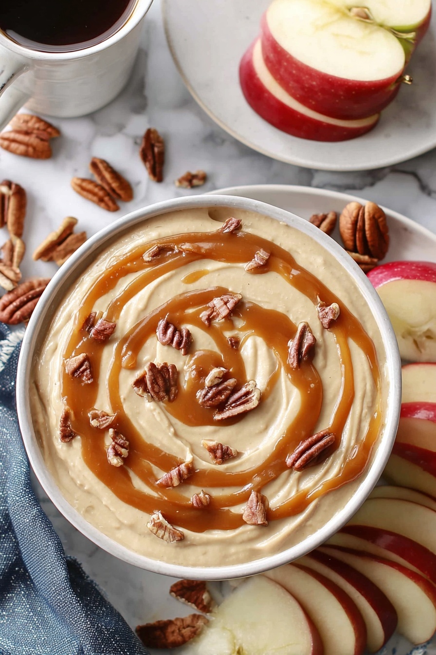 Caramel Cheesecake Dip, caramel cheesecake dip, easy caramel dip, creamy fruit dip, caramel dessert dip - A white bowl holds a creamy beige dip that fills it nearly to the top, with smooth swirls of caramel sauce drizzled in a loose spiral on the surface. Small pieces of brown pecans are scattered evenly over the caramel, adding texture and contrast. Around the bowl, slices of red apple with white insides sit beside whole pecans. In the background, a white plate holds more apple slices, and a white marbled surface surrounds everything. A woman's hand holds a white cup filled with a dark drink near the top left corner. photo taken with an iphone --ar 2:3 --v 7