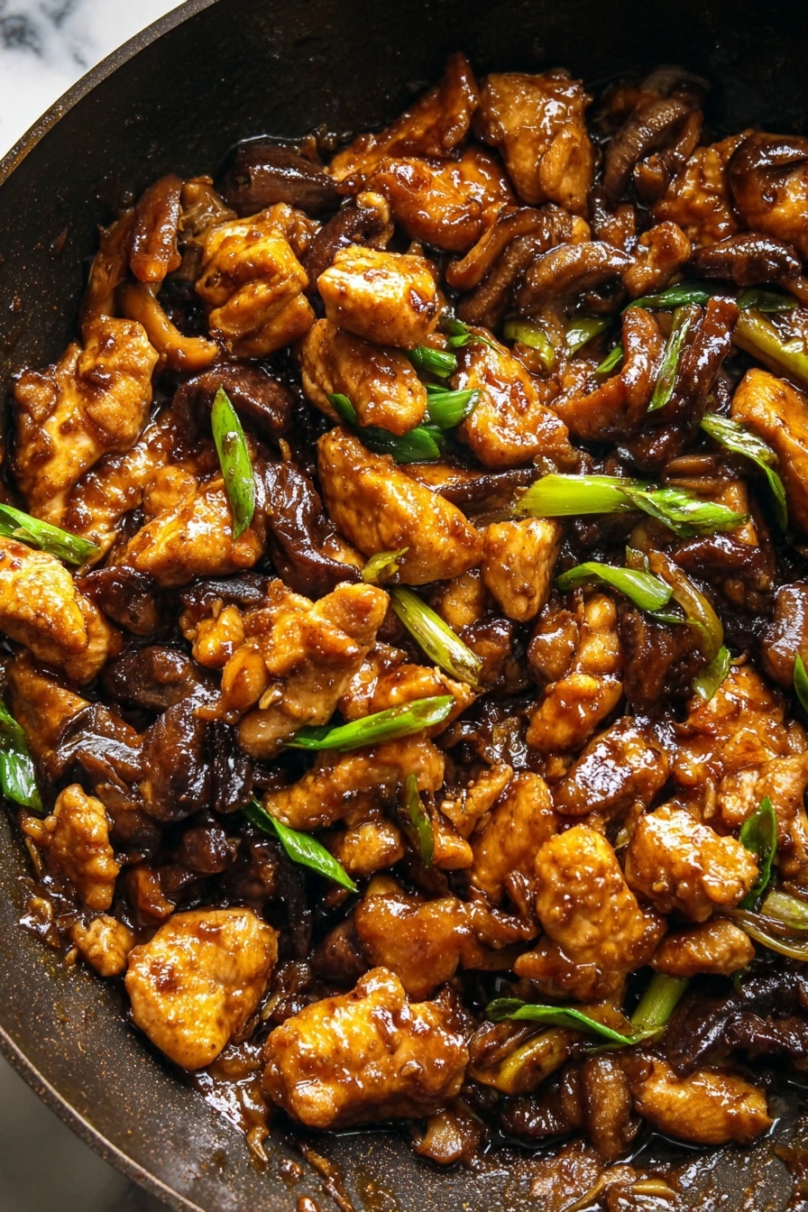 Black Pepper Mushroom Chicken Stir Fry, mushroom chicken stir fry, black pepper chicken, easy Asian stir fry, quick weeknight dinner - The image shows a close-up of a dark pan filled with a rich brown stir-fry dish. The stir-fry has several layers of golden brown cooked chicken pieces that look crispy on the edges, mixed with dark brown cooked mushroom slices. Scattered throughout the dish are small pieces of bright green sliced spring onions, adding a fresh contrast. The sauce covering the ingredients is glossy and thick, giving the dish a shiny look. The background is a white marbled texture. photo taken with an iphone --ar 2:3 --v 7