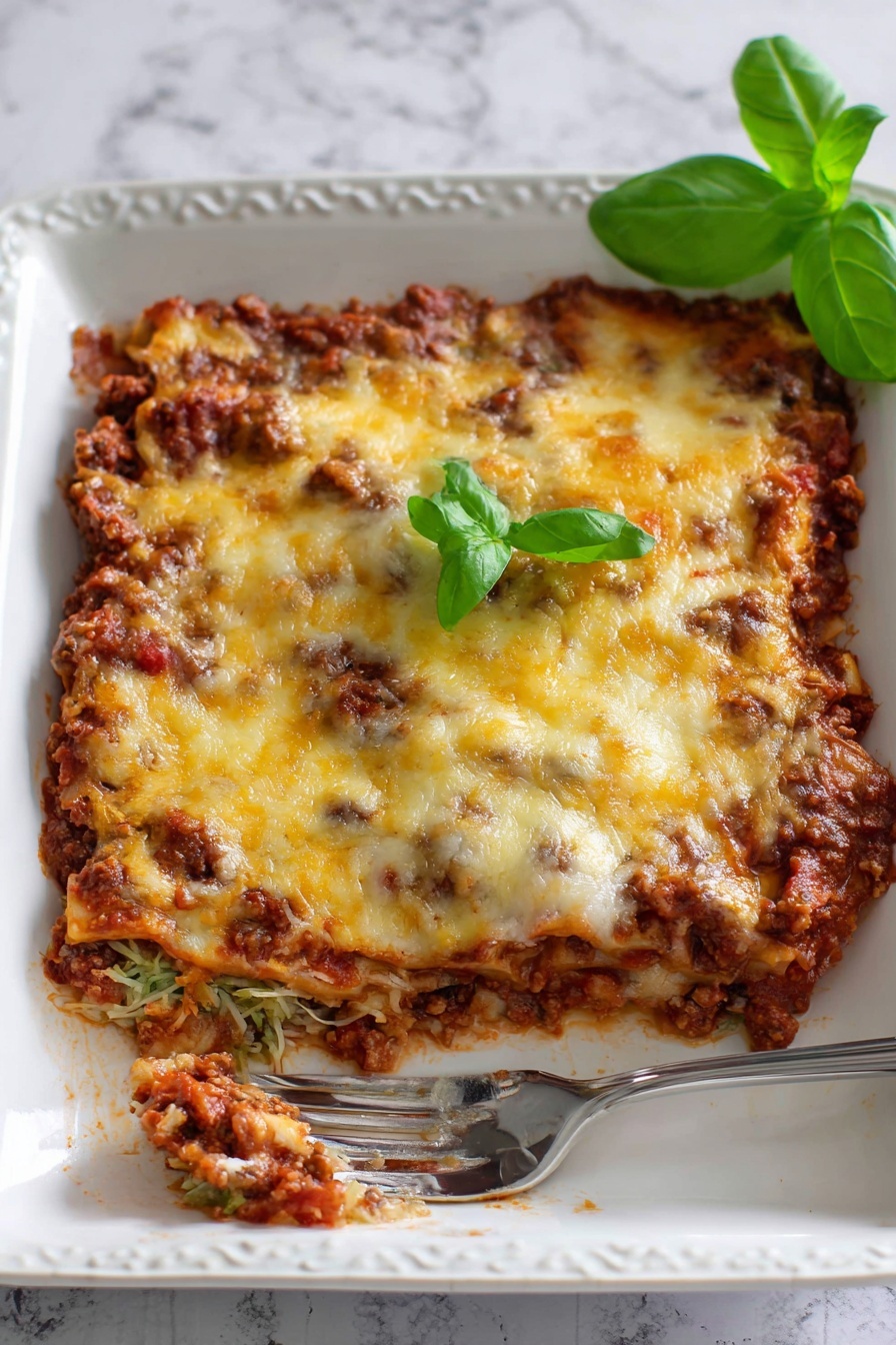 Zucchini Pizza Casserole, healthy zucchini casserole, easy zucchini dinner, veggie-packed pizza casserole, zucchini dinner recipes - The image shows a white rectangular baking dish filled with a baked casserole that has three visible layers. The bottom layer is a chunky, dark brown meat sauce mixed with red tomato sauce creating a textured base. The middle layer is mostly hidden but looks to be another portion of meat sauce. The top layer is melted cheese with a mix of pale white and golden yellow colors, slightly browned in spots. Small green basil leaves are scattered on top, adding color contrast. In the bottom left corner, a metal spatula with a white handle is partially inserted under the casserole, revealing the inside layers and the rich texture of the dish. The dish is set on a white marbled surface. Photo taken with an iphone --ar 2:3 --v 7