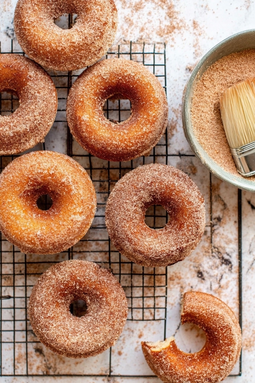 Cinnamon Sugar Doughnuts, homemade doughnuts, fluffy cinnamon donuts, soft baked doughnuts, easy cinnamon sugar treat - Seven cinnamon sugar donuts are arranged loosely on a black wire cooling rack. Each donut has a smooth, light brown surface coated with a fine layer of cinnamon sugar that gives a slightly grainy texture. The donuts have a soft, round shape with a distinct hole in the middle, and their edges are gently rounded. The cooling rack sits on a white marbled surface, which contrasts softly with the warm colors of the donuts. photo taken with an iphone --ar 2:3 --v 7