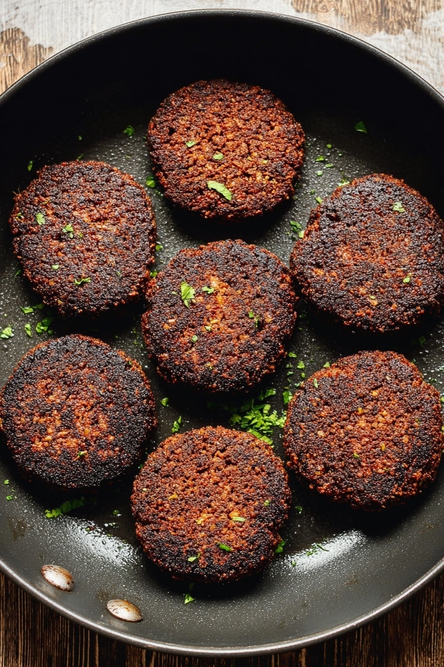Vegan Breakfast Sausage Patties, plant-based sausage patties, vegan breakfast recipes, dairy-free sausage, vegetarian breakfast ideas - The image shows eight dark brown, crispy patties arranged evenly inside a black round pan. The patties have a coarse texture with some small bits visible, and are sprinkled lightly with small green herb pieces. The background surface seen at the top is wooden but will be imagined as a white marbled texture. The pan has a slightly shiny area where the light reflects. photo taken with an iphone --ar 2:3 --v 7