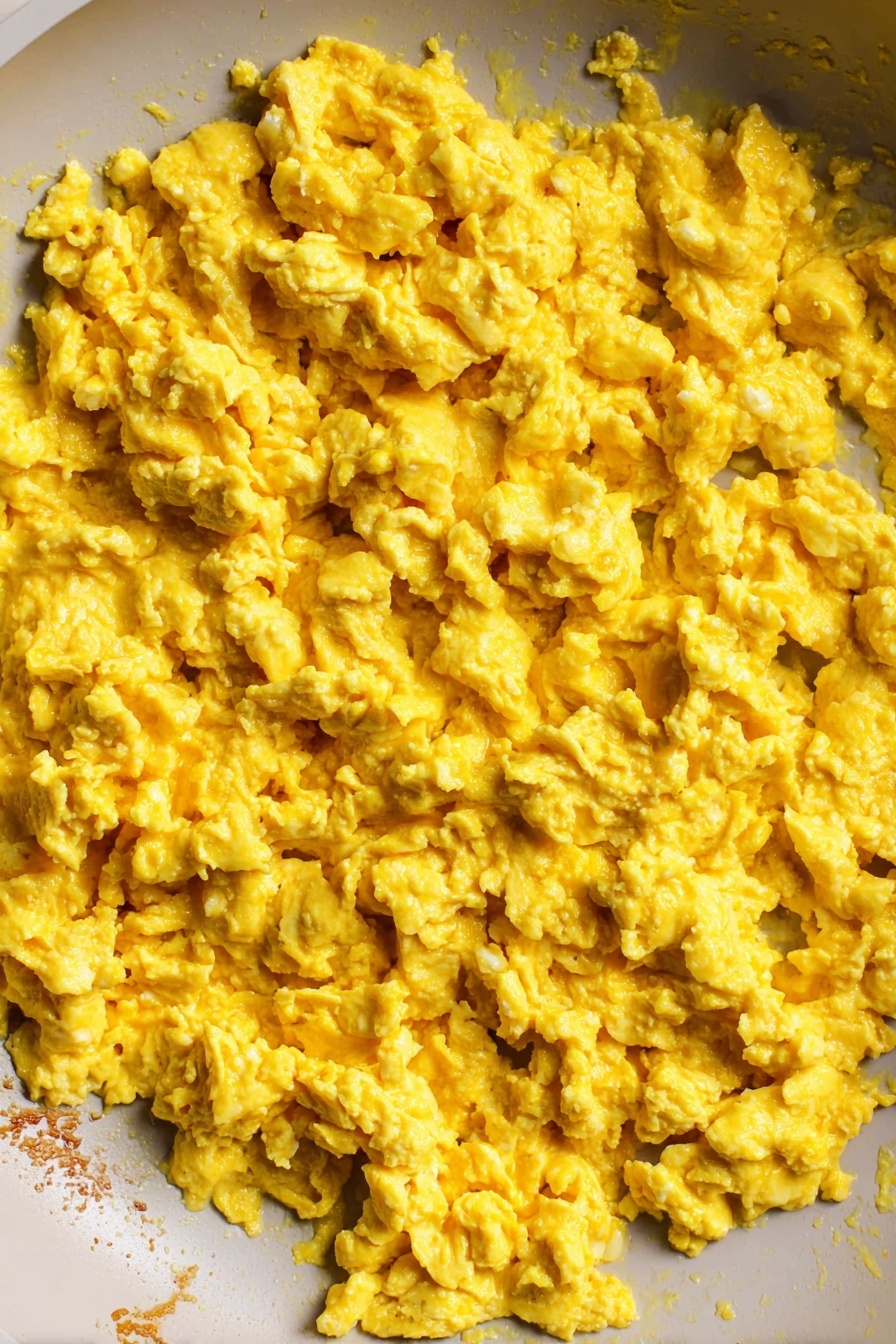 The Best Tofu Scramble, tofu scramble, vegan breakfast ideas, easy healthy breakfast, plant-based recipes - The image shows a close-up view inside a white pan filled with scrambled eggs. The cooked eggs have a soft, slightly chunky texture with a bright yellow color spread evenly across the pan. The edge of the pan reveals some lightly browned bits where the eggs touched the surface. The background is a white marbled texture. photo taken with an iphone --ar 2:3 --v 7