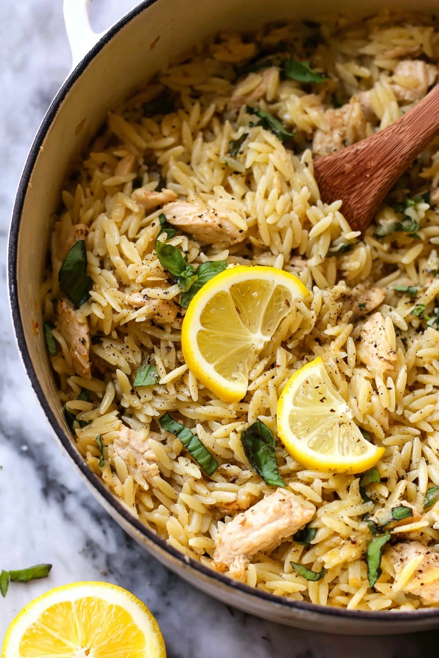 Lemon Chicken and Orzo, Lemon Chicken and Orzo recipe, Easy lemon chicken pasta, Quick chicken and orzo dinner, Bright lemon chicken dish - The image shows a white pot filled with cooked orzo pasta mixed with small pieces of light brown chicken and fresh green basil leaves scattered throughout. Two bright yellow lemon slices rest on top as a garnish, and there are visible specks of black pepper sprinkled across the dish. A wooden spoon stirs the orzo on the right side, and a lemon wedge is blurred in the white marbled background. The texture of the orzo looks soft and slightly shiny, mixing well with the tender chicken pieces. photo taken with an iphone --ar 2:3 --v 7
