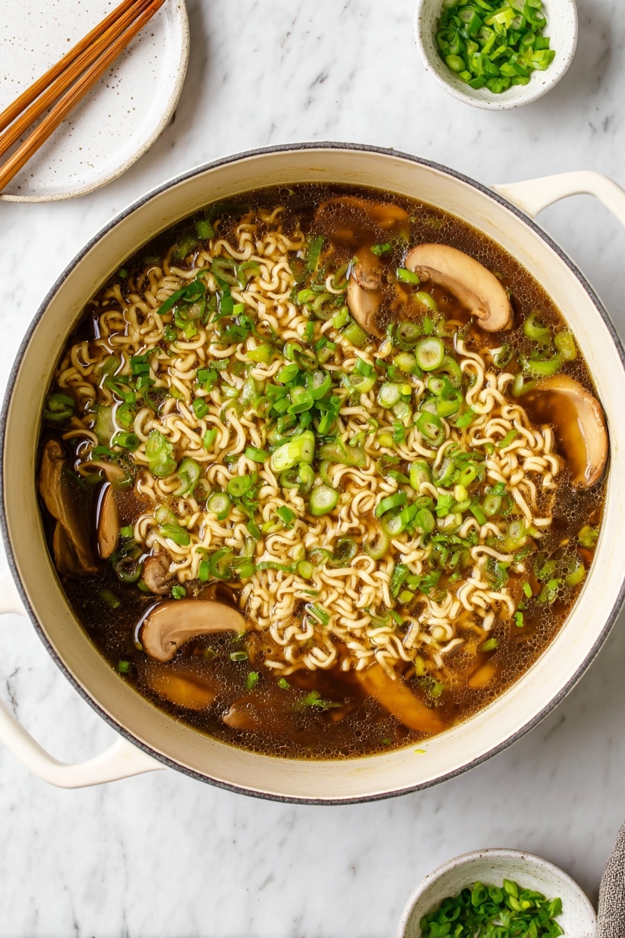 Easy Vegan Ramen, vegan ramen recipe, plant-based ramen, simple vegan noodle bowl, healthy vegan soup - A large white pot filled with dark brown broth containing light beige cooked curly noodles scattered throughout. Several slices of light brown mushrooms float on top, mixed with plenty of bright green chopped scallions spread evenly across the surface. The pot handles are visible on the sides, resting on a white marbled surface. In the background, a round white plate with wooden chopsticks rests towards the top left, and a small white bowl with extra chopped scallions sits on a matching saucer towards the top right. photo taken with an iphone --ar 2:3 --v 7