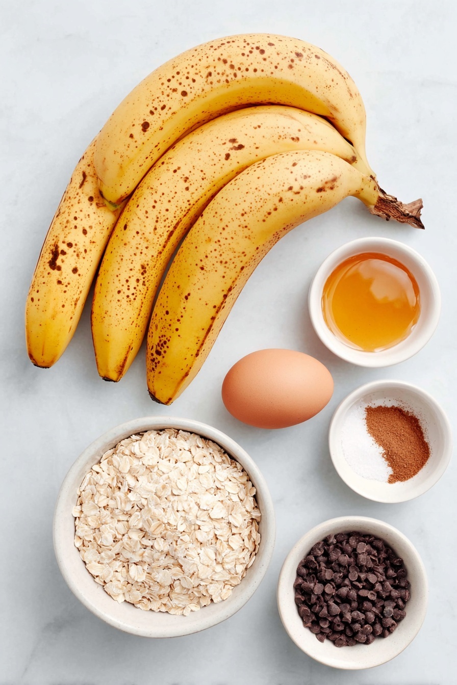 Banana Oatmeal Cookies with Chocolate Chips, healthy banana oatmeal cookies, easy fruit cookies, wholesome oatmeal treats, chocolate chip banana cookies - Flat lay of three overripe yellow bananas with brown spots, a small white ceramic bowl of golden honey, one whole uncracked brown egg, a small white ceramic bowl filled with quick cooking oats, a small white ceramic bowl containing ground cinnamon powder, a small white ceramic bowl of fine sea salt, and a small white ceramic bowl holding dark chocolate chips, all arranged with perfect symmetry and balanced proportions placed on a clean white marble surface, soft natural light, photo taken with an iPhone, professional food photography style, fresh ingredients, white ceramic bowls, no bottles, no duplicates, no utensils, no packaging --ar 2:3 --v 7 --p awthu7i m7354615311229779997