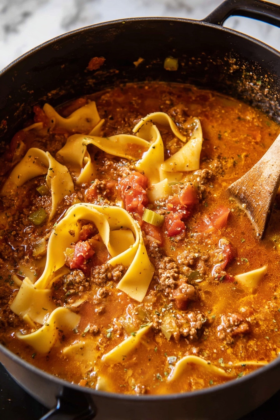 Spicy Lasagna Soup, spicy lasagna soup recipe, comforting lasagna soup, easy lasagna soup, weeknight lasagna soup - A black pot filled with thick lasagna soup showing several wide, flat, yellow pasta sheets, some curled and some straight, floating on a rich, chunky tomato-based broth with visible pieces of ground meat, diced red tomatoes, and bits of green celery. The soup has a slightly oily, speckled surface with herbs and spices, and steam rises gently from the hot mixture. A wooden spoon is partly submerged on the right side, stirring the soup. The pot is positioned against a white marbled background. photo taken with an iphone --ar 2:3 --v 7