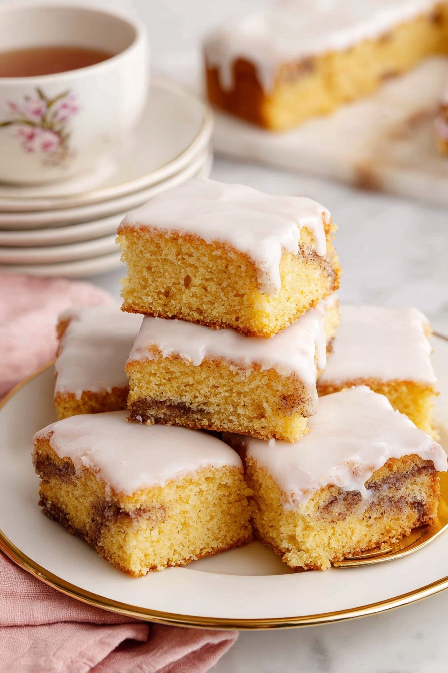 Cinnamon Roll Cake, Easy Cinnamon Roll Cake, No-Fail Cinnamon Roll Cake, Cinnamon Swirl Cake, Breakfast Cinnamon Cake - The image shows a close-up of a square piece of cinnamon roll cake with three layers: a light golden brown cake base with swirls of dark cinnamon running through the middle, topped with a thick, white creamy icing that smoothly covers the top and slightly drips down the sides. The piece sits on a small, white plate with delicate floral and butterfly decorations and a thin gold rim. In the background, there is a white plate with several more pieces of the same cake stacked slightly on top of each other. To the right, a white teacup with a gold rim and small bee design is filled with dark tea. A gold fork lies on a soft pink cloth to the side, and all items rest on a white marbled textured surface. photo taken with an iphone --ar 2:3 --v 7