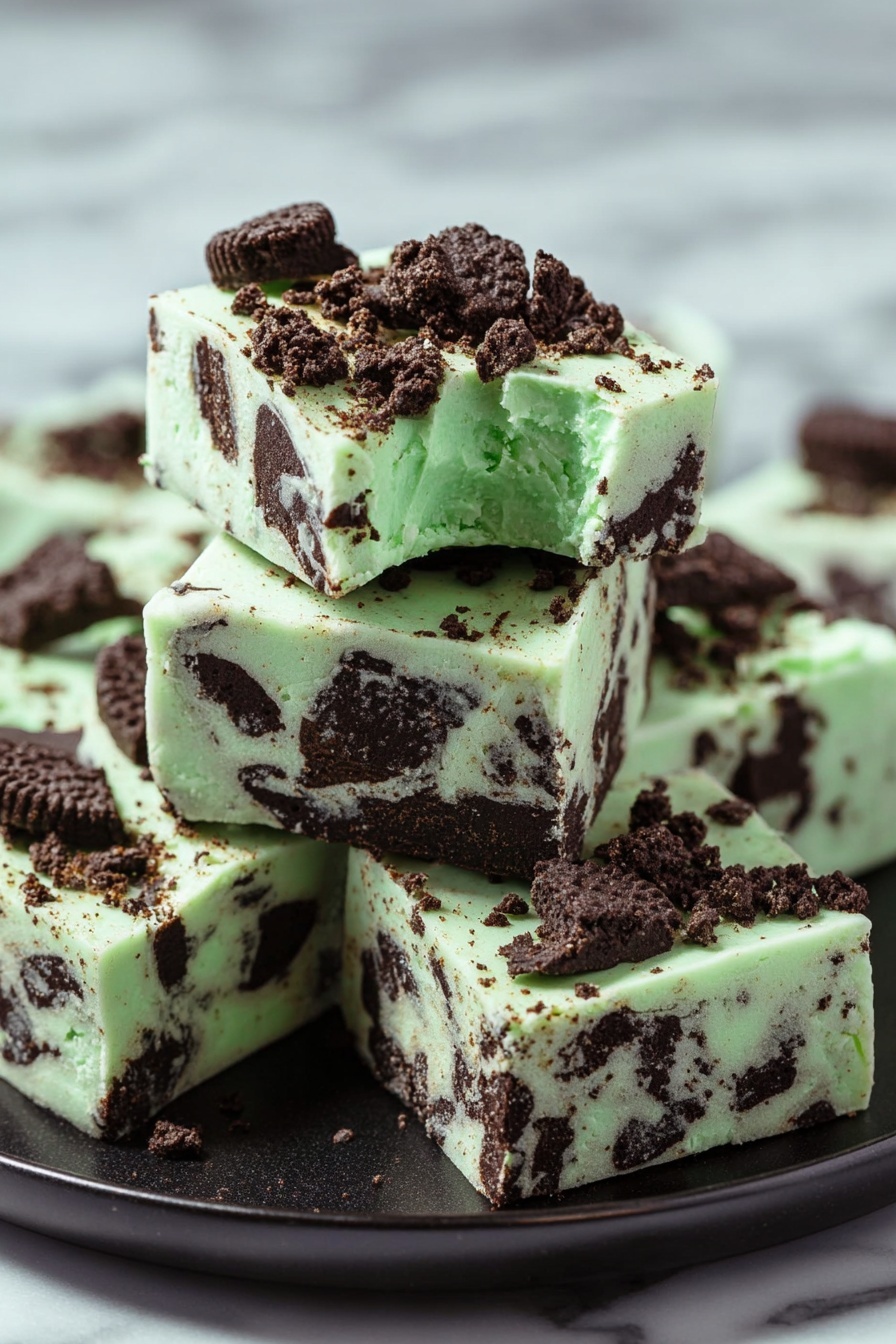 Mint Oreo Fudge, mint Oreo dessert, easy mint fudge, white chocolate fudge with Oreos, holiday mint fudge - The image shows a stack of five square pieces of mint chocolate fudge on a black plate, placed on a white marbled surface. The fudge has a pale green base with dark brown chunks of cookie mixed in all layers. On the top, bigger cookie pieces and crumbs are scattered, adding texture and color contrast. Each piece is thick and smooth with distinct edges, and the top piece has a small bite taken from its corner, showing a creamy interior with visible cookie pieces inside. Photo taken with an iphone --ar 2:3 --v 7
