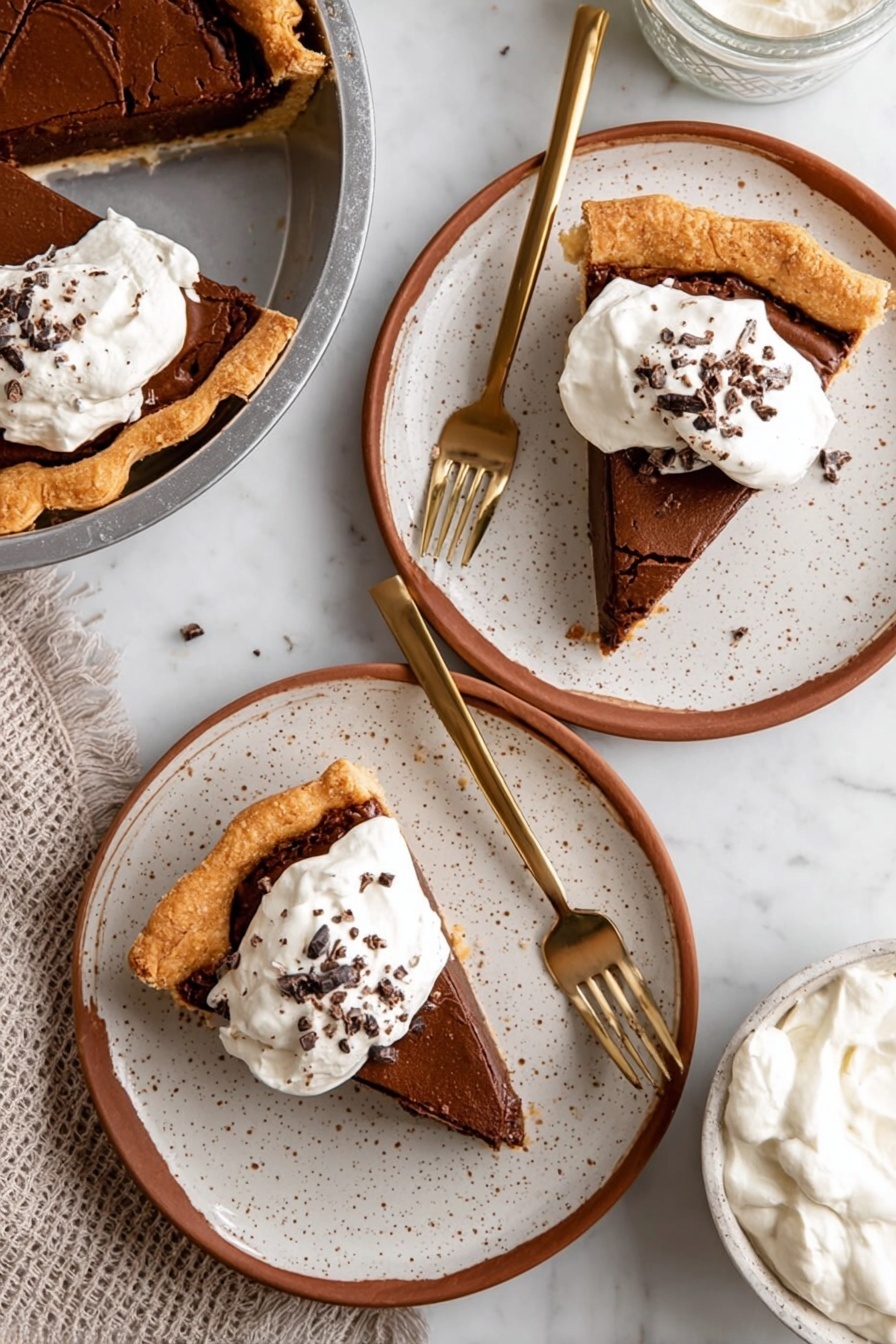 Fudgy Chocolate Brownie Pie, chocolate brownie pie, chocolate dessert, decadent brownie pie, easy chocolate pie - A slice of chocolate pie with three visible layers sits in a metal pie pan: the bottom layer is a light golden flaky crust, the middle layer is a thick dark brown chocolate filling, and the top layer is a cracked lighter brown chocolate crust. On top of the slice is a dollop of white whipped cream sprinkled with small chocolate shavings. The pie pan rests on a metal cooling rack over a white marbled surface. In the background, there is a blurred white container and a white bowl with more chocolate pie. photo taken with an iphone --ar 2:3 --v 7