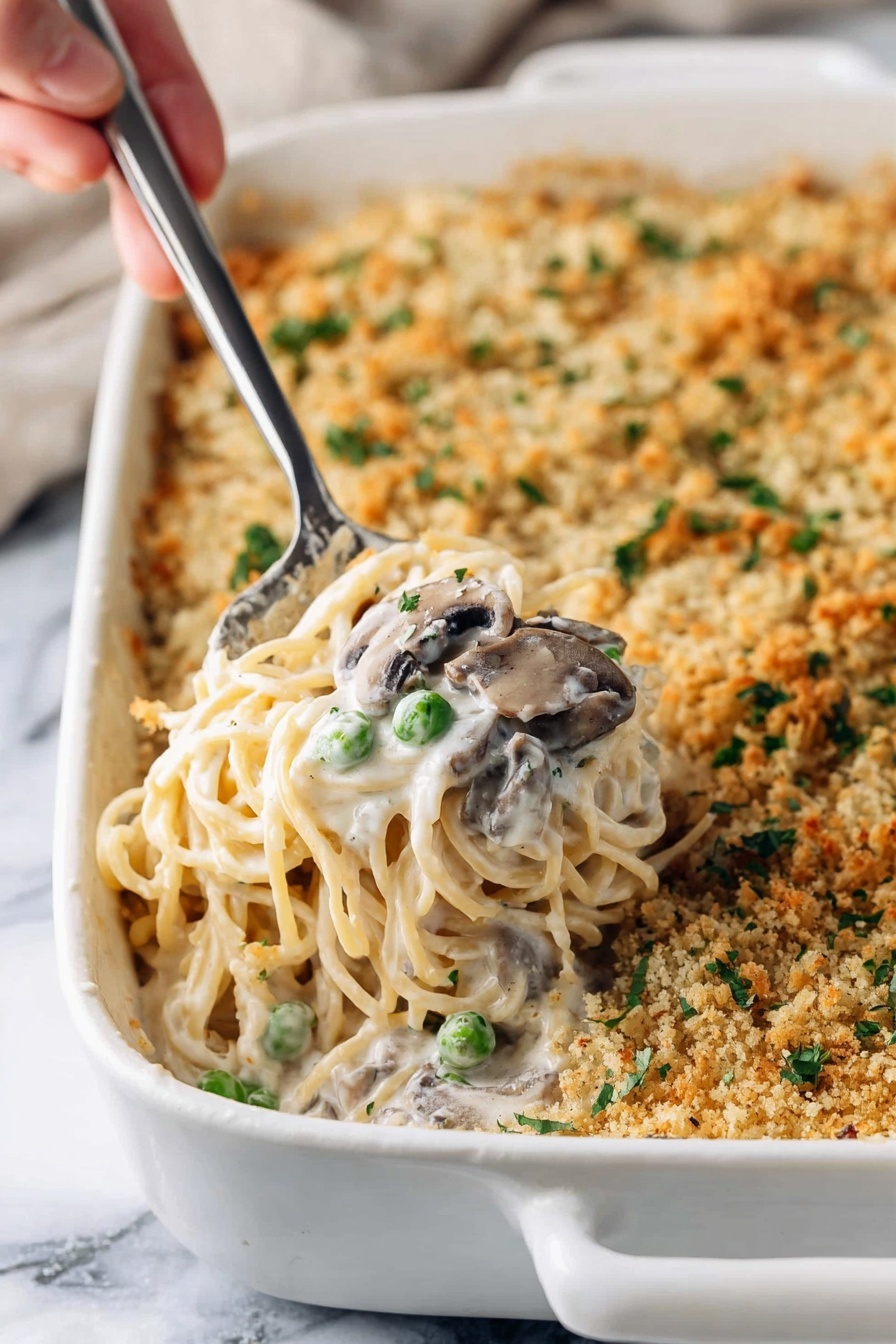 Creamy Turkey Tetrazzini, turkey pasta casserole, comforting turkey pasta dish, easy creamy turkey recipe, holiday leftover turkey dinner - A white baking dish filled with creamy spaghetti casserole topped with a golden brown crumb layer that has small green herb pieces sprinkled on it; a woman's hand holds a metal serving spoon lifting a portion showing soft spaghetti noodles mixed with white cream sauce, green peas, and sliced mushrooms, all nestled in the middle of the dish; the white marbled surface beneath adds a clean contrast to the warm colors of the casserole, photo taken with an iphone --ar 2:3 --v 7