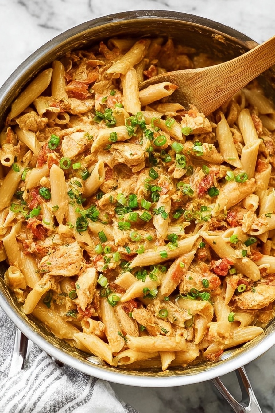 Creamy Cajun Chicken Pasta, Cajun Chicken Pasta, Creamy Chicken Pasta, One-Pot Cajun Pasta, Spicy Cajun Chicken - A close-up view of a large silver pan filled with creamy pasta made with short tube-shaped noodles, chopped light brown cooked chicken pieces, and a rich tan-colored sauce. Mixed in are small bits of red tomatoes and sprinkled chopped green onions on top to add bright green color contrast. A light wooden spoon rests inside the pan on the right side, partially covered by the pasta. The pan is placed on a white marbled surface with a white and gray striped cloth beneath the handle. The dish looks warm and inviting with a mix of soft textures and fresh garnish. Photo taken with an iphone --ar 2:3 --v 7