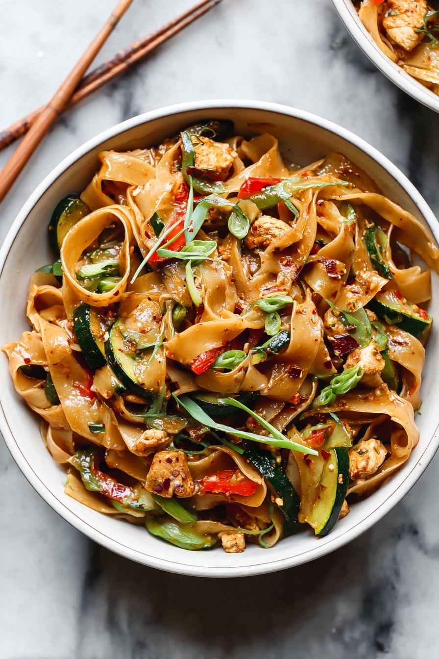 Drunken Noodles, Thai Drunken Noodles, Spicy Stir-Fry, Easy Noodles Recipe, Chicken and Vegetable Noodles - The image shows a close-up of a pan filled with wide, flat pasta noodles mixed with green vegetables and small red pieces. The pasta is light brown, and the green vegetables include sliced green beans and some leafy parts. The red pieces appear to be small chunks of tomatoes or peppers. The texture looks slightly glossy from a light sauce coating the pasta and vegetables. The background is a white marbled surface. Photo taken with an iphone --ar 2:3 --v 7