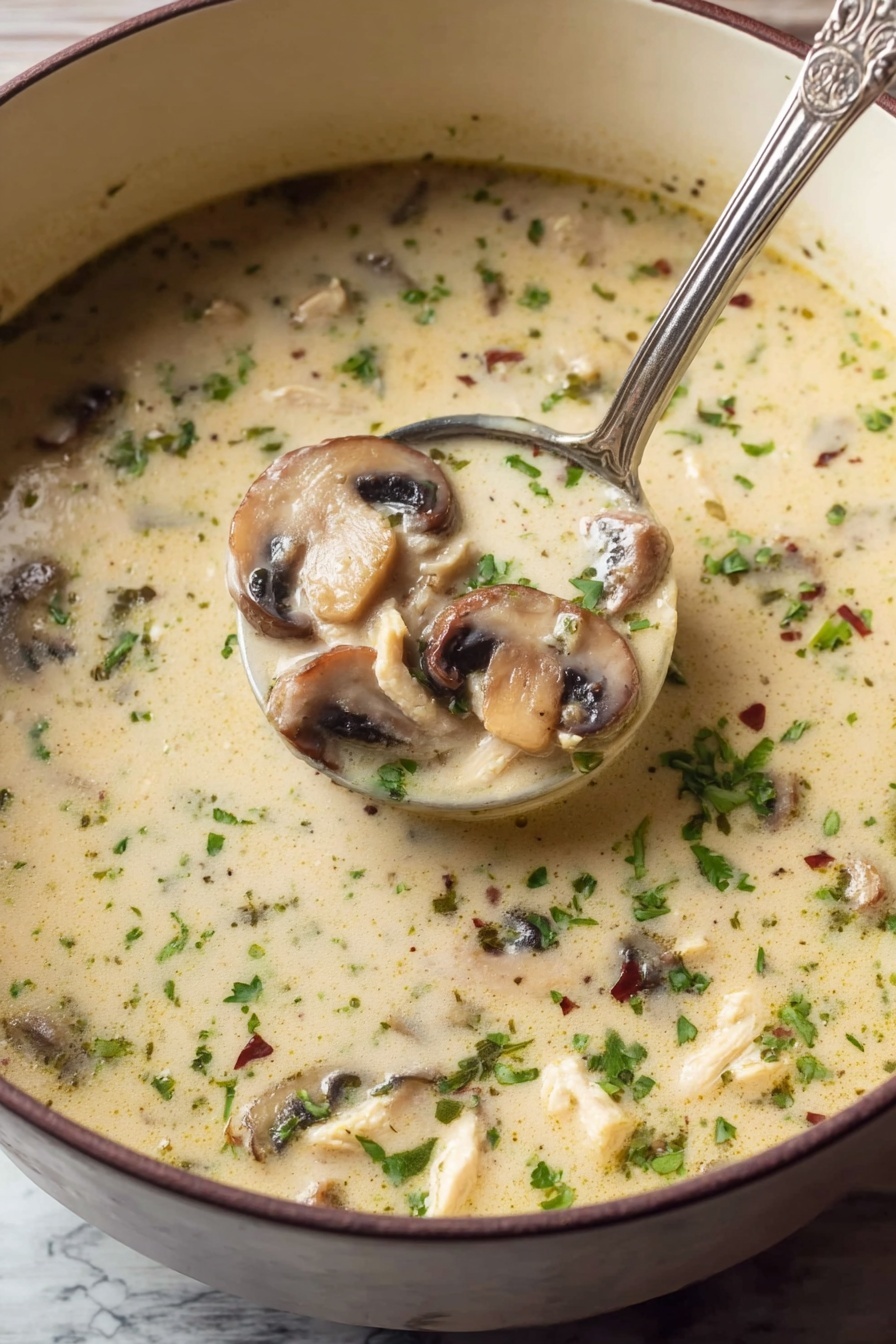 Creamy Chicken Mushroom Soup, Chicken Mushroom Soup recipe, comforting mushroom soup, easy chicken and mushroom soup, hearty creamy soup - A close-up view of a light creamy soup filled with sliced mushrooms and small pieces of chicken, sprinkled with chopped green herbs and tiny dried herbs throughout. The soup has a smooth texture with floating bits of green and brown, and a silver ladle scoops a portion showing three layers of sliced mushrooms, chicken bits, and the creamy broth all mixed. The soup is in a deep white bowl, resting on a white marbled surface. Photo taken with an iphone --ar 2:3 --v 7