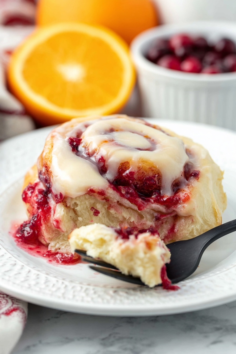 Cranberry Orange Sweet Rolls, cranberry orange sweet rolls, citrus cranberry rolls, holiday breakfast rolls, easy cranberry orange buns - The dish shows a soft, swirled roll with three main layers: a creamy white icing layer on top that looks smooth and rich, a middle layer with a light beige dough, and a bright red layer of berry filling that appears juicy and slightly thick, seeping out from the roll. The roll is on a white plate with gentle embossed patterns, against a white marbled background. In the front, a black fork holds a small piece of the roll with some berry filling and dough, and in the back, blurred slices of orange and a white bowl filled with deep red cherries add color contrast. Photo taken with an iphone --ar 2:3 --v 7